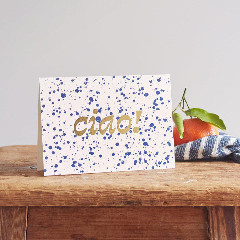 Card with 'ciao!' text on a wooden surface with a blurred background