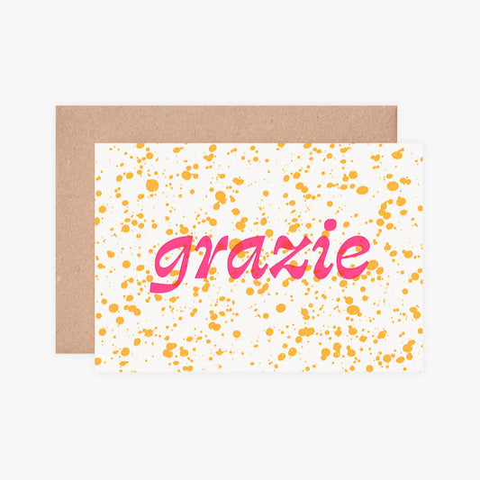 Greeting card with 'grazie' text and yellow dots on a white background, accompanied by a brown envelope.